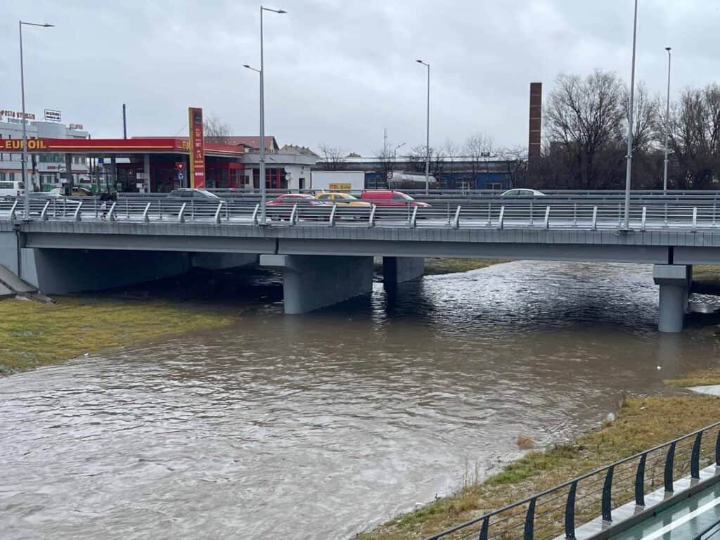 Râul Cibin cu debit crescut și apă tulbure, curgând pe sub un pod rutier din Sibiu